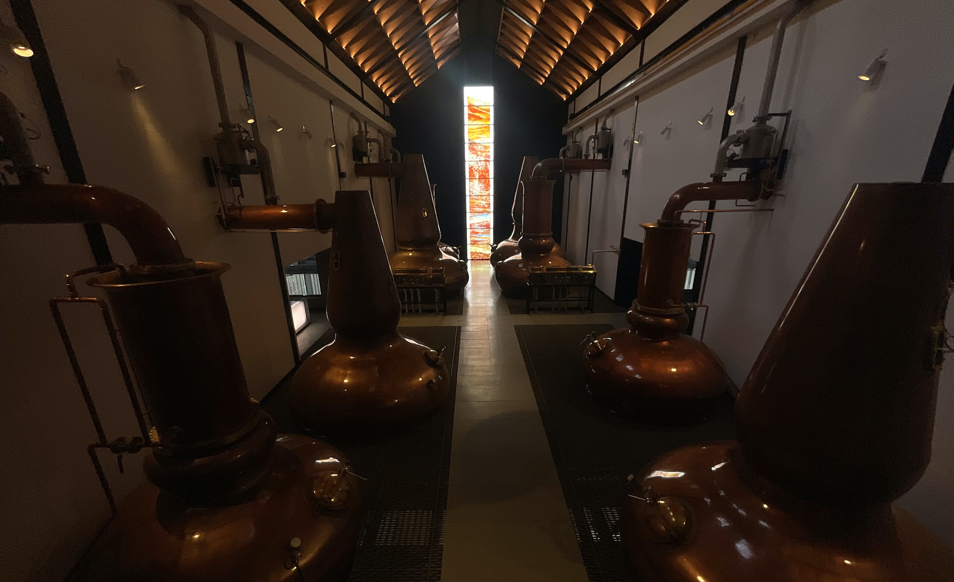 The Dalmore Still House — four pairs of copper stills with the fused glass window glowing at the far end, Alness, Scotland